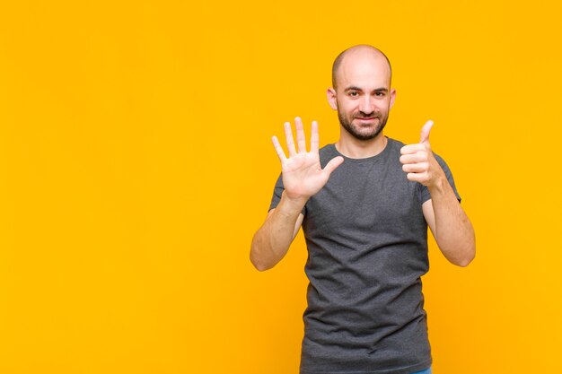 Uomo calvo sorridente e dall'aspetto amichevole, mostrando il numero sei o sesto con la mano in avanti, conto alla rovescia