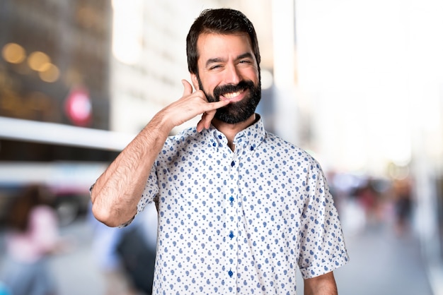 Uomo castana bello con la barba che fa gesto del telefono