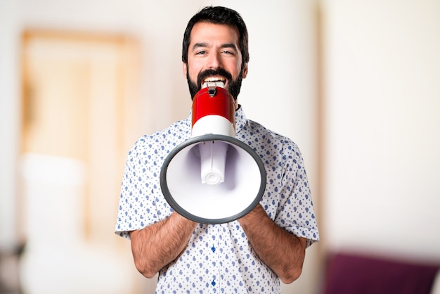 Uomo castana bello con la barba che grida dal megafono