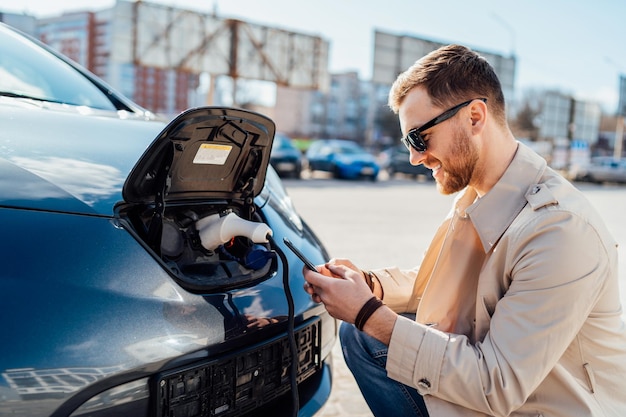 Uomo casual con smartphone vicino all'auto elettrica