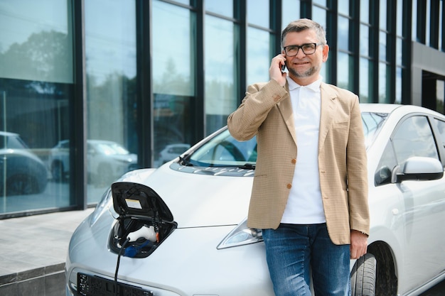 Uomo casual vicino all'auto elettrica in attesa della fine del processo di ricarica della batteria