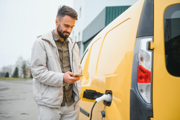 Uomo casual vicino all'auto elettrica in attesa della fine del processo di ricarica della batteria