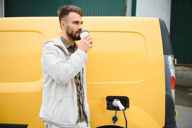 Uomo casual vicino all'auto elettrica in attesa della fine del processo di ricarica della batteria