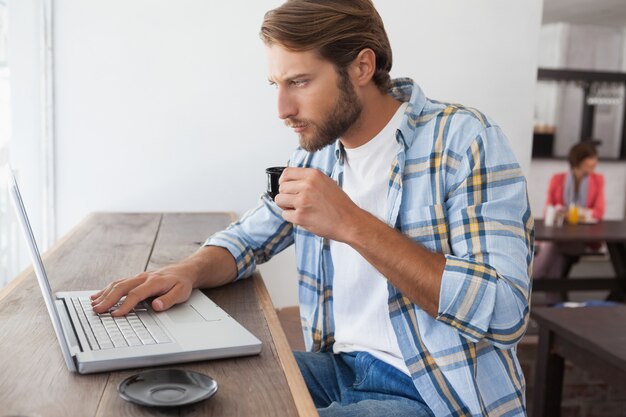 Uomo casuale che per mezzo del computer portatile che beve caffè espresso