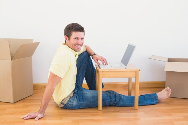 Uomo casuale che si siede sul pavimento facendo uso del computer portatile sul tavolino da salotto a casa