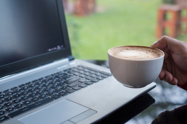 Uomo casuale che tiene tazza di caffè con il computer portatile in ufficio