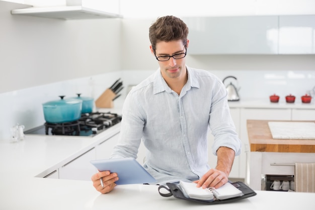 Uomo casuale con tavoletta digitale utilizzando un diario in cucina