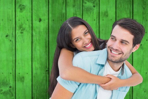 Uomo casuale felice che dà la ragazza graziosa piggy back contro le plance di legno verde brillante