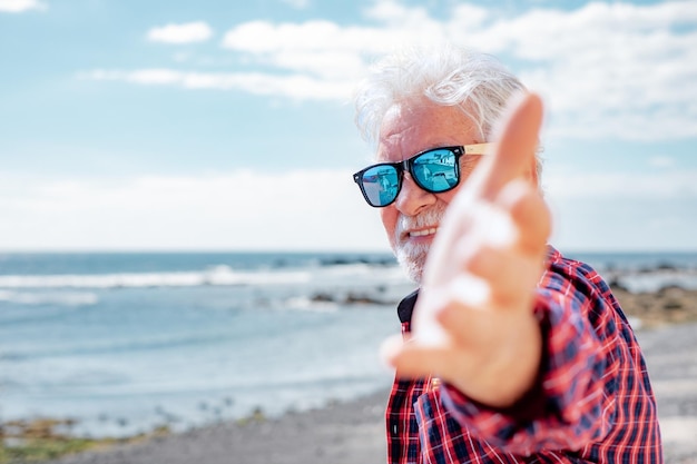 Uomo caucasico anziano felice che guarda l'obbiettivo in piedi sulla spiaggia in vacanza al mare o in pensione