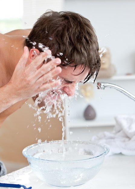 Uomo caucasico attraente che spruzza acqua sul suo fronte dopo la rasatura nel bagno