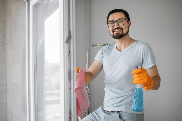 Uomo caucasico barbuto in occhiali seduto su una scala a pioli che tiene una spugna per lavare le finestre