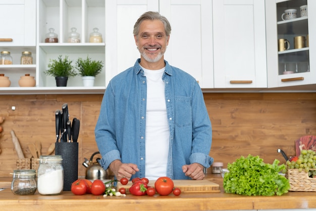 Uomo caucasico bello maturo dai capelli grigi in piedi nella cucina luminosa.