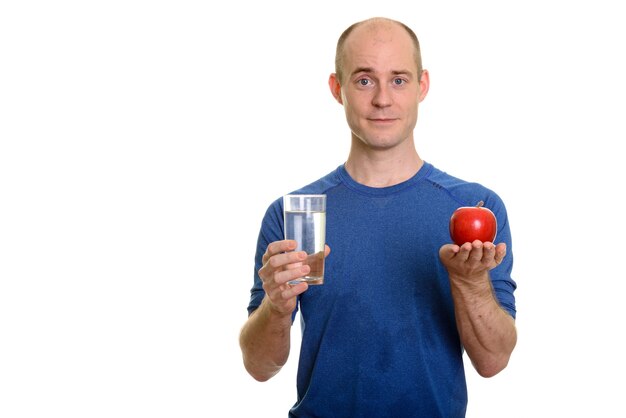 Uomo caucasico calvo che tiene bicchiere d'acqua e mela rossa