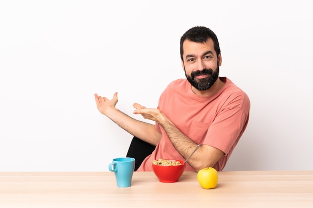 Uomo caucasico che fa colazione in un tavolo che estende le mani di lato per invitare a venire.