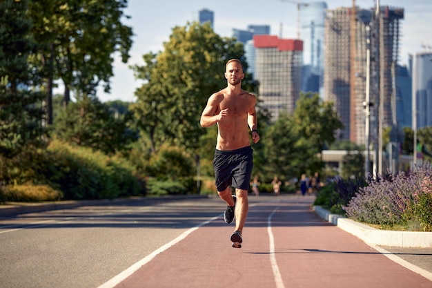 Uomo caucasico che fa jogging sulla pista da corsa L'atleta maschio biondo in allenamento allo stadio corre in una giornata di sole primaverile o estiva concetto di stile di vita sano di persone reali