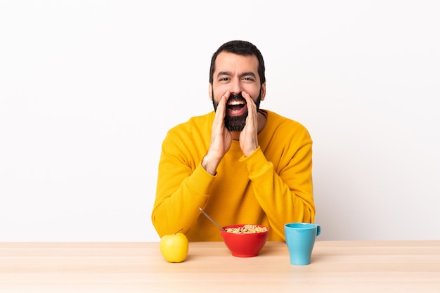 Uomo caucasico che mangia prima colazione in una tabella che grida e che annuncia qualcosa