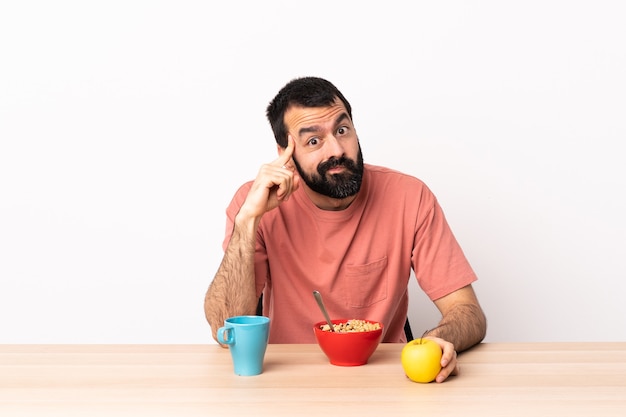 Uomo caucasico che mangia prima colazione in una tabella che pensa un'idea.