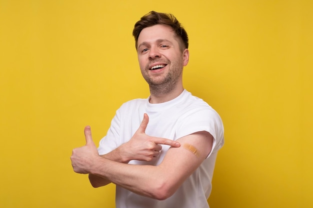 Uomo caucasico che mostra il suo braccio vaccinato Ha ricevuto un vaccino corona guardando la fotocamera Studio girato su parete gialla