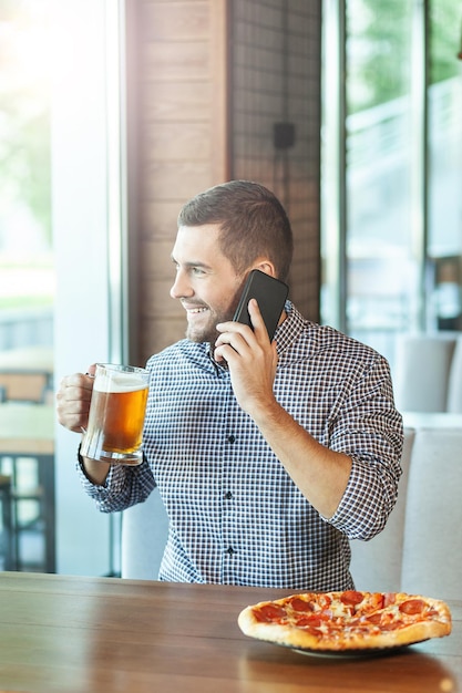 Uomo caucasico che parla sullo smartphone e beve birra al bar
