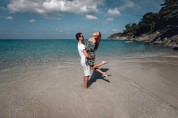 Uomo caucasico che porta la sua ragazza dai capelli rossi godendosi un tardo pomeriggio insieme in spiaggia. Phuket. Tailandia.