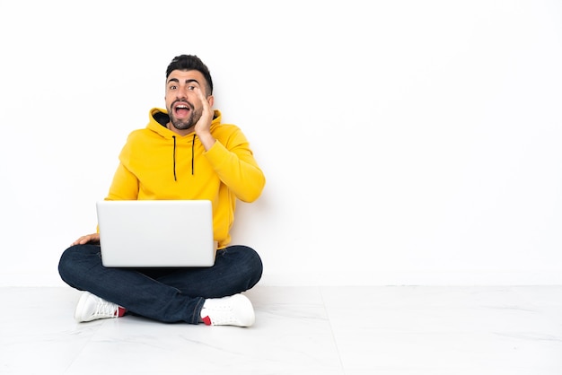 Uomo caucasico che si siede sul pavimento con il suo computer portatile che grida con la bocca spalancata