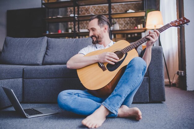 Uomo caucasico che suona la chitarra seduto sul pavimento a casa