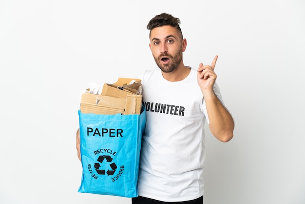 Uomo caucasico che tiene un sacchetto di riciclaggio pieno di carta da riciclare isolato su bianco che intende realizzare la soluzione sollevando un dito