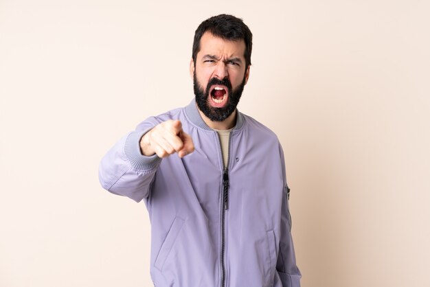 Uomo caucasico con la barba che indossa una giacca sopra il muro isolato frustrato e indicante la parte anteriore