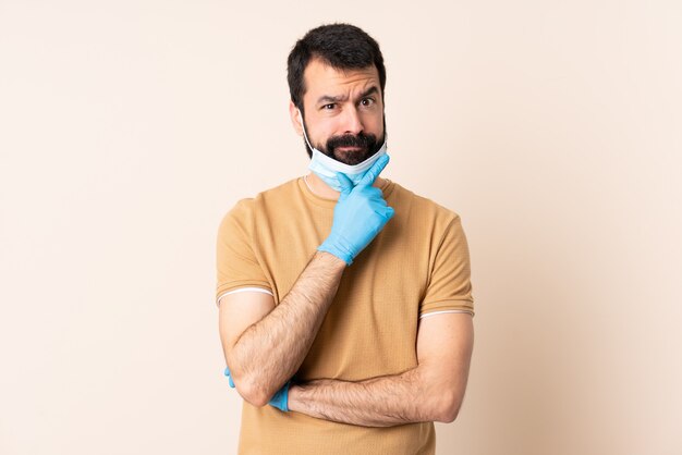 Uomo caucasico con la barba che protegge con una maschera e guanti sopra il pensiero della parete