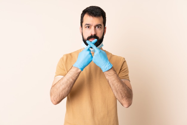 Uomo caucasico con la barba che protegge con una maschera e guanti sopra la parete isolata che fa gesto di arresto con la sua mano per fermare un atto