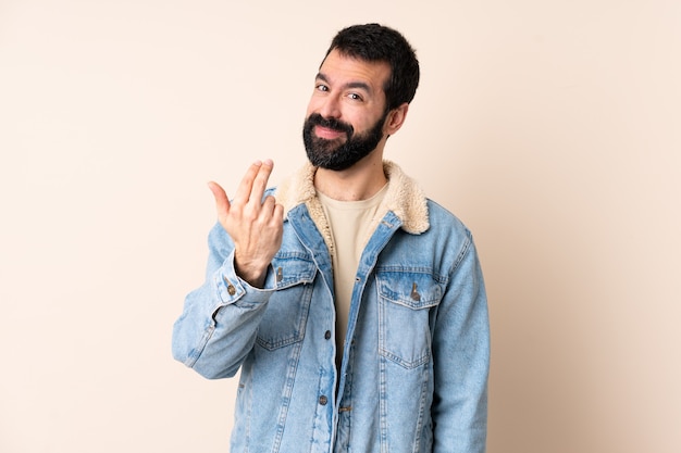 Uomo caucasico con la barba sopra la parete isolata che invita a venire con la mano.