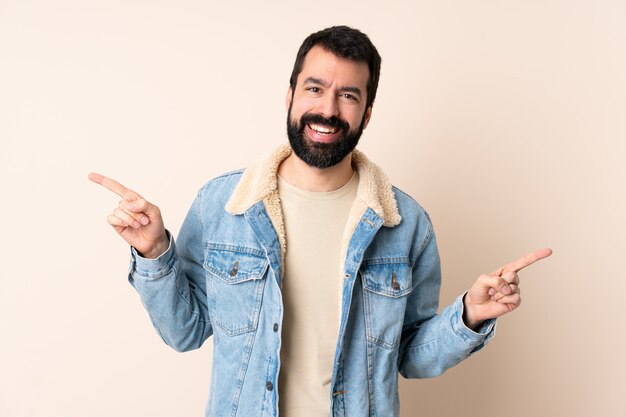 Uomo caucasico con la barba sulla parete isolata che punta il dito verso i laterali e felice