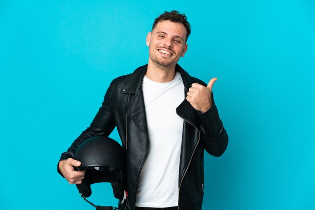 Uomo caucasico con un casco da motociclista isolato su blu che punta di lato per presentare un prodotto