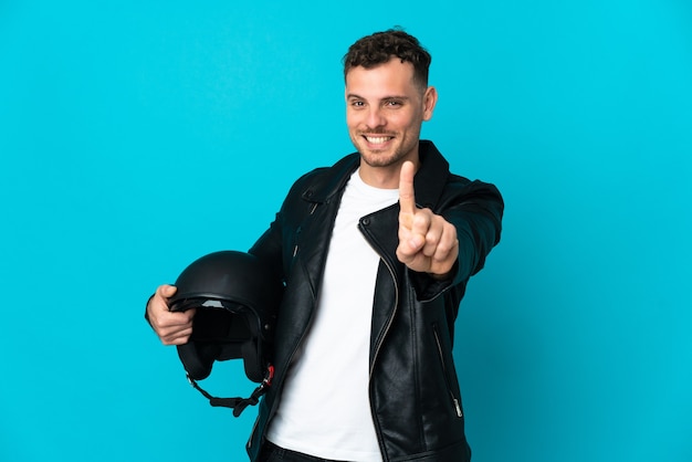 Uomo caucasico con un casco da motociclista isolato sulla parete blu che mostra e alza un dito