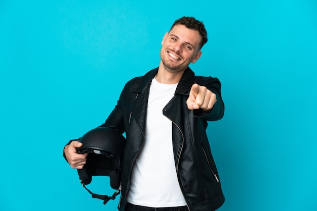 Uomo caucasico con un casco da motociclista isolato sulla parete blu che punta davanti con felice espressione