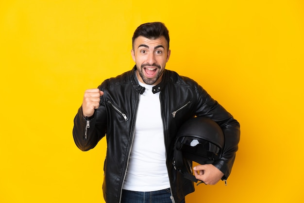 Uomo caucasico con un casco da motociclista sopra la parete gialla isolata che celebra una vittoria nella posizione del vincitore