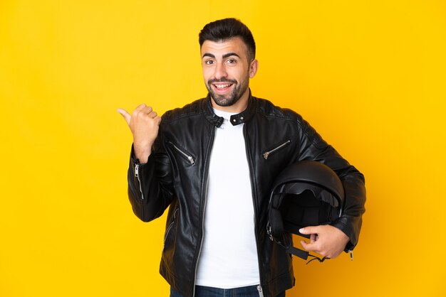 Uomo caucasico con un casco da motociclista su sfondo giallo isolato che punta di lato per presentare un prodotto