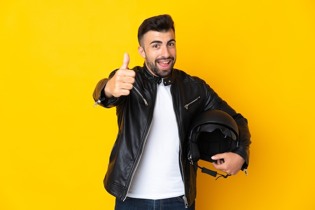 Uomo caucasico con un casco da motociclista su sfondo giallo isolato con i pollici in su perché è successo qualcosa di buono