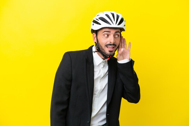 Uomo caucasico d'affari con un casco da bici isolato su sfondo giallo che ascolta qualcosa mettendo la mano sull'orecchio