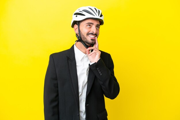 Uomo caucasico d'affari con un casco da bici isolato su sfondo giallo pensando a un'idea mentre guarda in alto