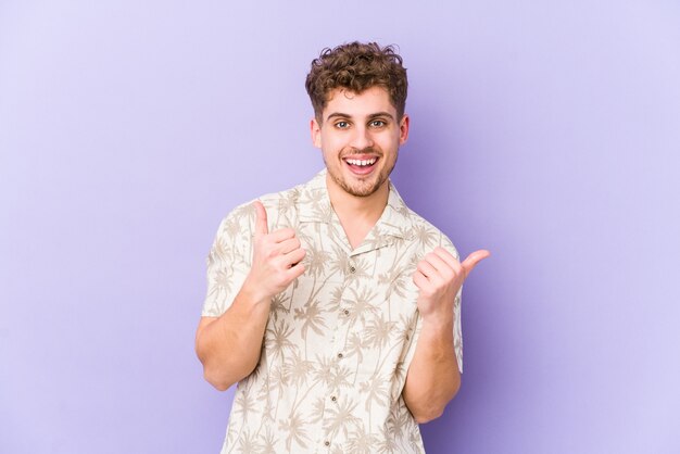 Uomo caucasico dei giovani capelli ricci biondi isolato sollevando entrambi i pollici in su, sorridendo e sicuro.