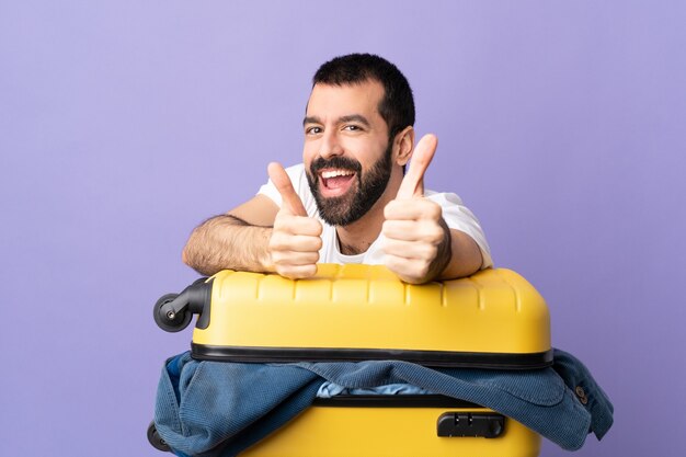 Uomo caucasico del viaggiatore con una valigia piena di vestiti sopra la porpora isolata