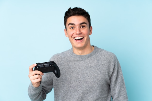 Uomo caucasico dell'adolescente che gioca con un regolatore del videogioco isolato sul blu