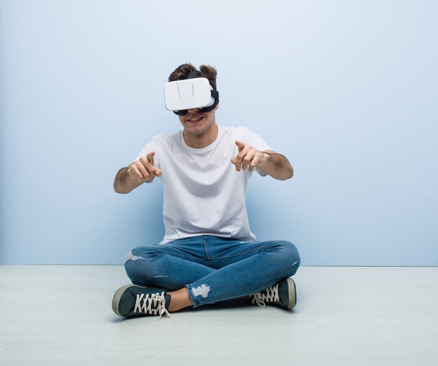 Uomo caucasico dell'adolescente che usando i vetri di una realtà virtuale che si siedono sul pavimento