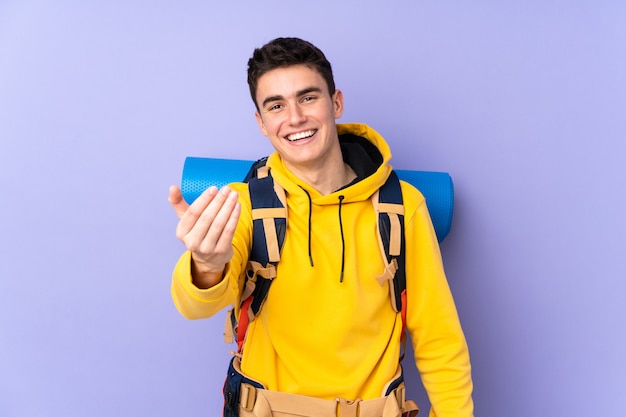 Uomo caucasico dell'alpinista dell'adolescente con un grande zaino sulla parete porpora che invita a venire