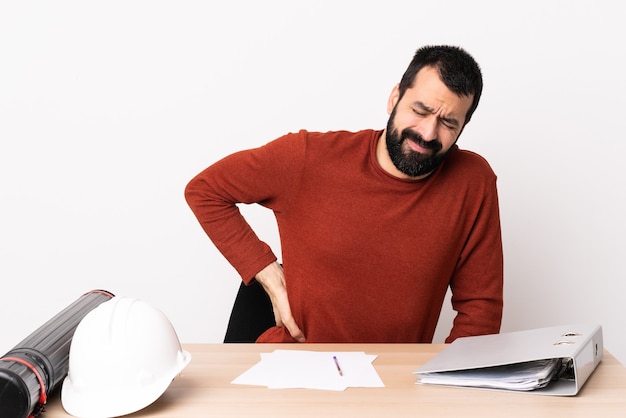 Uomo caucasico dell'architetto con la barba in un tavolo che soffre di mal di schiena per aver fatto uno sforzo.