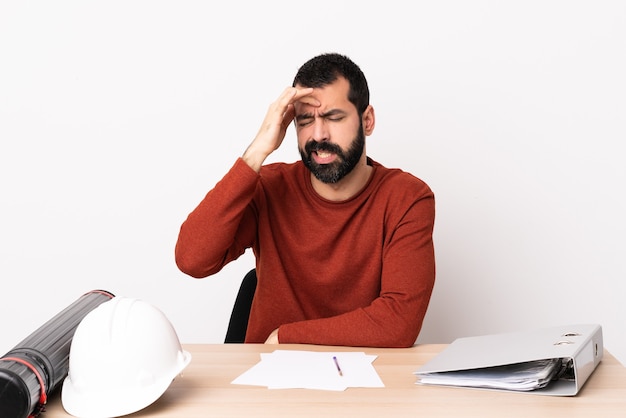 Uomo caucasico dell'architetto con la barba in un tavolo con mal di testa