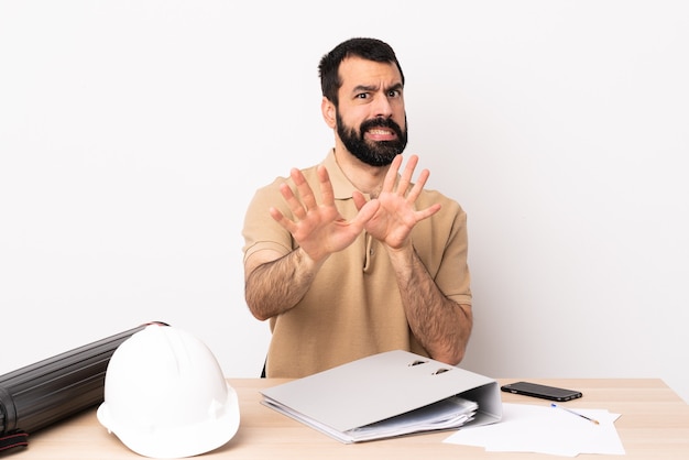 Uomo caucasico dell'architetto con la barba in un tavolo nervoso che allunga le mani in avanti.