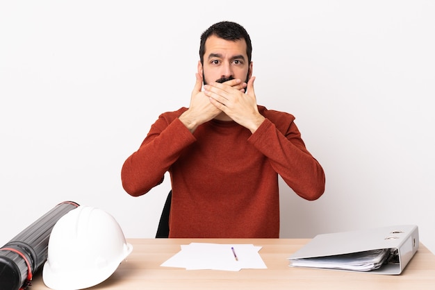 Uomo caucasico dell'architetto con la barba in una bocca coning della tabella con le mani.