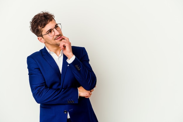 Uomo caucasico di affari giovane isolato sul muro bianco rilassato pensando a qualcosa guardando uno spazio di copia.